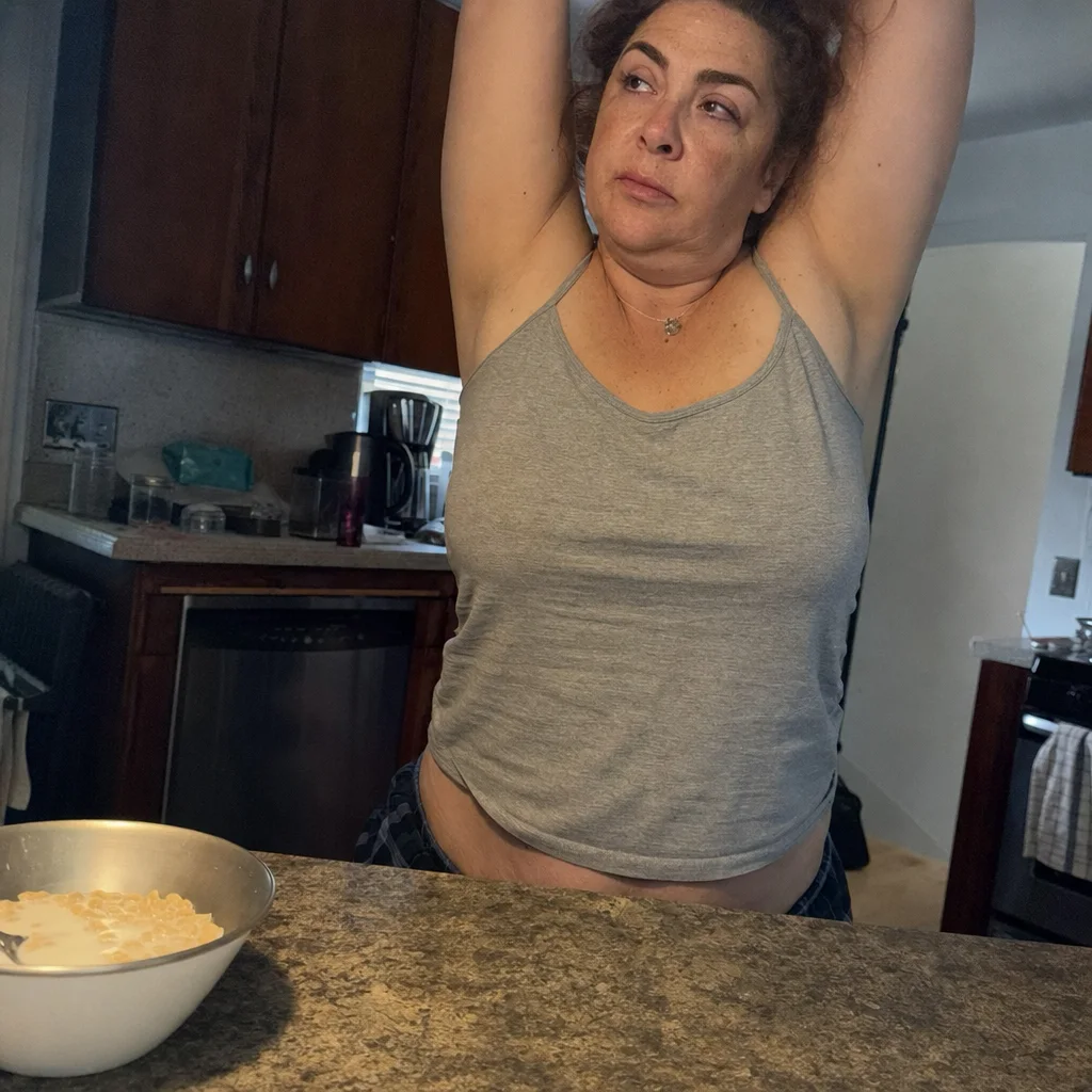 Woman stretching both arms overhead beside breakfast in a home kitchen.